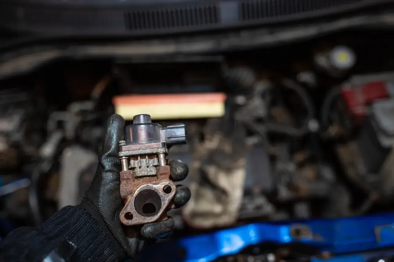 Zardzewiały zawór EGR w rękawicy mechanika. To pokazuje skutki jazdy z niesprawnym zaworem EGR w nowoczesnym dieslu, prowadzące do uszkodzeń.