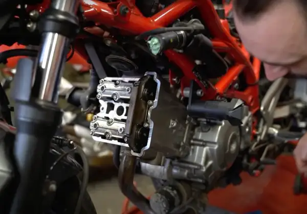 Mechanik sprawdza zawory motocykla, przygotowując się do zadania: jak samodzielnie ustawić luzy zaworowe w motocyklu.