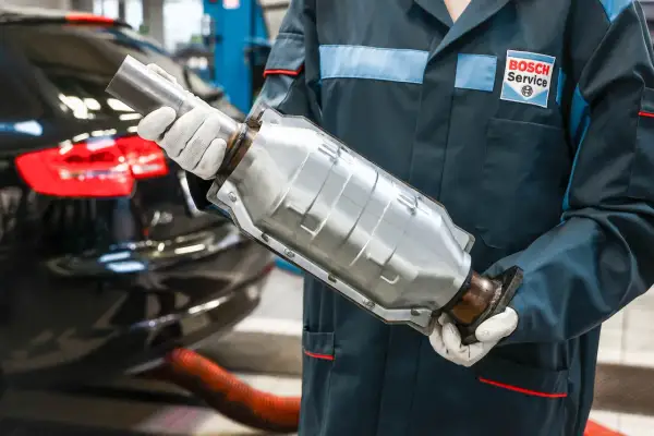 Mechanik w rękawiczkach trzyma katalizator. Usunięcie go w benzynie może wpłynąć na moc silnika, ale też na środowisko.
