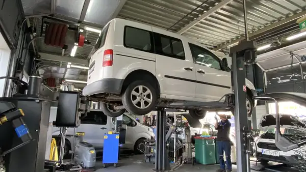 Warsztat samochodowy. Mechanik pracuje pod białym vanem na podnośniku. Prawdziwe powody dla których serwisy odmawiają montażu części dostarczonych przez klienta.