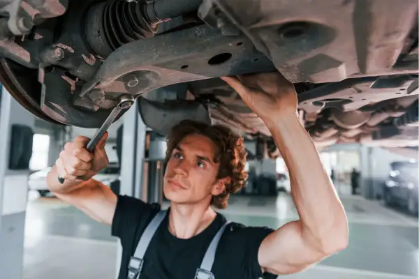 Mechanik naprawia zawieszenie, by uniknąć skutków jazdy z wybitą tuleją wahacza przedniego.