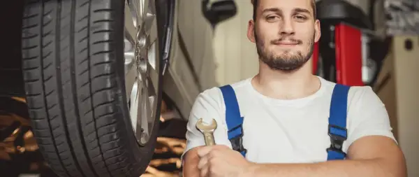 Uśmiechnięty mechanik z kluczem w dłoni, gotowy do pracy przy aucie hybrydowym. To on stoi za nowymi certyfikatami dla mechaników.